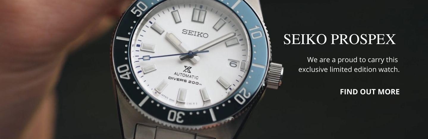 Seiko watch laying on a wooden desk beside a notebook and pen.