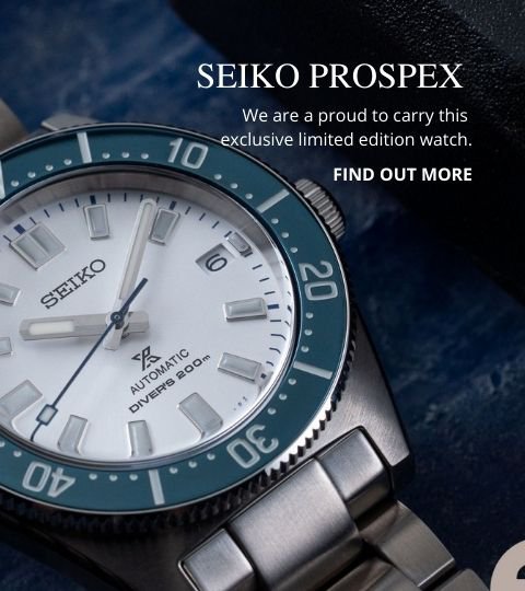 Seiko watch laying on a wooden desk beside a notebook and pen.